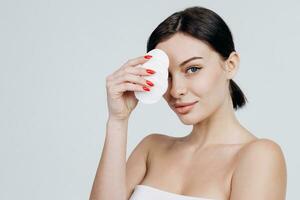 retrato de un joven atractivo mujer limpieza su cara con un algodón almohadilla aislado terminado blanco antecedentes. Perfecto Fresco piel. puro belleza modelo. cuidado concepto. foto