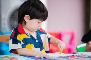 bebé chico es haciendo Arte pintura con lápices de color. preescolares son aprendizaje a hogar escuela. vacío espacio a entrar texto. un 2 año antiguo niño usa brillantemente de colores ropa. foto