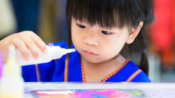 Asian girl holds white watercolor bottle and stares at bottle's mouth. Child doing water painting art. photo