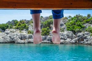 Bare feet hanging from wooden pier over sea water. Holiday vacation by the sea. photo