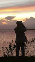 vertical vídeo do silhueta do uma homem em a lago às pôr do sol video