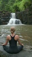lindo mulher prática meditação às uma cascata dentro a floresta tropical dentro Tailândia video