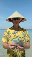 homme dans vietnamien chapeau compte le vietnamien dong sur tropical plage dans vietnam video