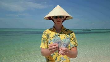 Man in Vietnamese hat counting the Vietnamese Dong on tropical beach in Vietnam video