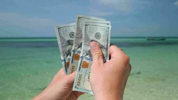 Hands counting US dollars on tropical beach. Close up video