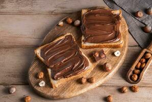 Board of bread with chocolate paste and hazelnuts on wooden background photo