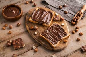 Board of bread with chocolate paste and hazelnuts on wooden background photo