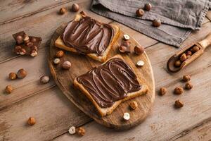 Board of bread with chocolate paste and hazelnuts on wooden background photo