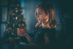 un linda niña en un negro vestir se sienta a un mesa con Mandarina. día festivo, nuevo año, Navidad foto