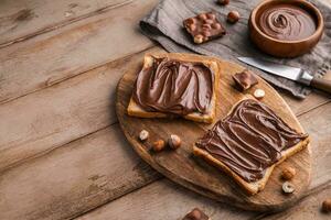 Board of bread with chocolate paste and hazelnuts on wooden background photo