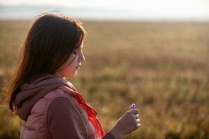 Cute teenage girl in the field on an autumn morning holding a cornflower flower in her hand photo