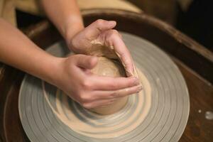 Potter girl works on potter's wheel, making ceramic pot out of clay in pottery workshop photo