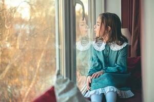 a pensive cute girl sits and looks out the window photo