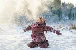 linda niña en el bosque en invierno lanza nieve foto