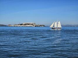 A sail boat crossing in front of Alcatraz Island in San Francisco California photo