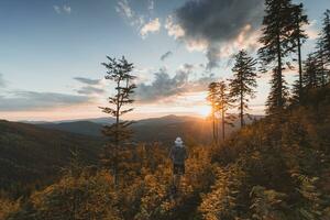 Enthusiastic hiker aged 50-55 with a hat standing on a stump watching the sunset in Beskydy mountains, Czech Republic. Hiking lifestyle photo