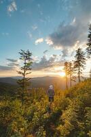 Enthusiastic hiker aged 50-55 with a hat standing on a stump watching the sunset in Beskydy mountains, Czech Republic. Hiking lifestyle photo