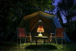 Clásico cabina carpa, antiguo petróleo lámpara en un de madera mesa con retro sillas. a noche en el bosque foto