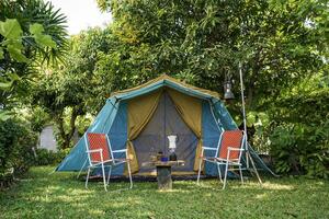 Clásico cabina carpa, antiguo petróleo lámpara, retro sillas, grupo de cámping carpas con al aire libre hacer cafe instalaciones en de madera mesas en un bosque cámping zona en el bosque. foto