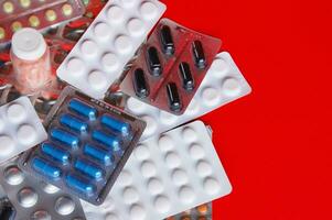 Assorted pharmaceutical medicine pills, tablets and capsules on red background photo