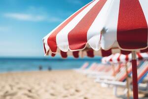 AI generated Close up image of a red and white vertical striped beach umbrella on a background of a beach with sun loungers and blue sea photo