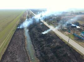 Burning dry grass along the irrigation canal. Smoke and the flame of dry grass. Burnt dry grass. photo