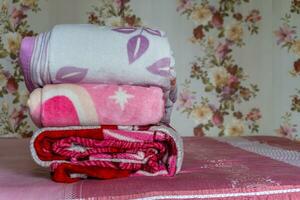Stacked of colorful blanket on pink bed. Folded pink blankets. White folded duvet lying photo