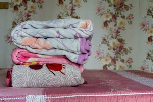 Stacked of colorful blanket on pink bed. Folded pink blankets. White folded duvet lying photo