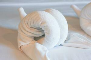 White towels on the bed in the hotel room are rolled up into the shape of an elephant's head. Soft, vintage tones. photo