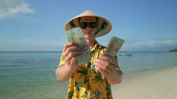 Man in Vietnamese hat counting the Vietnamese Dong on tropical beach in Vietnam video