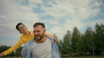 Happy fatherhood family smiling Caucasian male father joyful son piggyback dad back little boy child kid playing toy plane together pilot have fun flying fantasy outside field countryside park holiday video