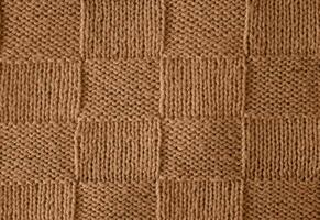 Texture of smooth knitted sweater with pattern. Handmade knitting wool or cotton fabric texture. Unusual abstract knitted chess pattern background texture. Peach Fuzz colour of 2024 year photo