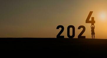 mujer participación en pie contento nuevo año 2024 concepto, silueta de mujer estar césped y éxito con hermosa puesta de sol antecedentes. contento nuevo año 2023 utilizar para web bandera y anuncio publicitario. foto