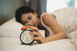 Close up alarm clock. woman sleeping in comfortable bed with silky linens in the morning. Women lying in bed and keeping eyes closed while covered with blanket. cheerful and comfortable. photo