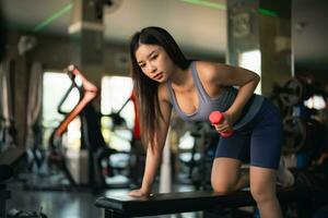 Asian fit sportswoman smiling and working out excercise weights with dumbbells at the fitness gym. asian woman wearing sportwear doing exercise to burn fat at gym. Sport woman fitness concept. photo