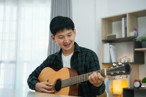 Asian man youtuber live streaming performance playing guitar and sing a song. Asian man teaching guitar and singing online. Musician recording music with laptop and playing acoustic guitar. photo