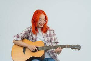 Smart asian woman red hair and wearing glasses musician play guitar on grey or white background. Guitarist music concept, asia women holding acoustic guitar look at the camera in the studio lighting. photo