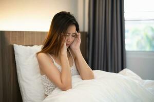 Depressed asian woman sadly sitting on the bed in the bedroom. Sad asian women suffering depression insomnia awake and sit alone on the bed in bedroom. Depression health people concept. photo