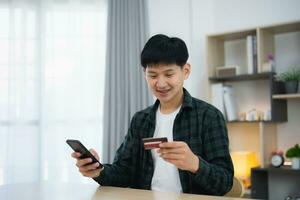 Man holding credit card and using mobile to shopping online. asian man working at home. Online shopping, e-commerce, internet banking, spending money, working from home concept. photo