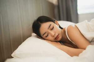 Asian woman sleeping with smart watch showing tracking heartbeat monitor in comfortable bed with silky linens at night light. Women lying in bed and keeping eyes closed while covered with blanket. photo