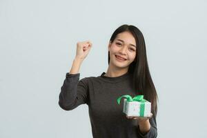 Asian woman with braces raise hand cheerful smiling happy and hold in hand present box with gift ribbon bow look aside isolated on grey background studio. Lifestyle concept. photo