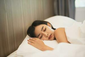 Asian woman sleeping with smart watch showing tracking heartbeat monitor in comfortable bed with silky linens at night light. Women lying in bed and keeping eyes closed while covered with blanket. photo