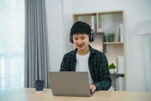 Smart Asian man wearing headphone with braces smiling working with computer laptop. Work form home. freelance life style, New normal social distancing lifestyle. Work form anywhere concept. photo