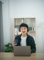 Smart Asian man wearing headphone with braces smiling working with computer laptop. Work form home. freelance life style, New normal social distancing lifestyle. Work form anywhere concept. photo