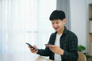 Man holding credit card and using mobile to shopping online. asian man working at home. Online shopping, e-commerce, internet banking, spending money, working from home concept. photo