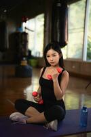 Asian fit sportswoman smiling and working out excercise weights with dumbbells at the fitness gym. asian woman wearing sportwear doing exercise to burn fat at gym. Sport woman fitness concept. photo