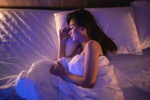 Asian woman sleeping in comfortable bed with silky linens at night light. Women lying in bed and keeping eyes closed while covered with blanket. Content and peaceful, cheerful and comfortable. photo