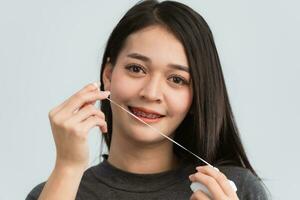 Asian woman braces using dental floss. Teeth braces on the white teeth of women to equalize the teeth. Bracket system in smiling mouth, close up photo teeth, macro shot, dentist health concept.