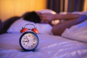 cerca arriba de alarma reloj. Deprimido mujer tristemente tendido en el cama en el dormitorio. triste asiático mujer sufrimiento depresión insomnio despierto y sentar solo en el cama en dormitorio. despertar arriba tarde. foto