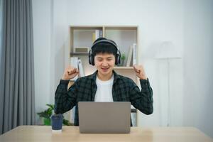 Smart Asian man wearing headphone with braces smiling raise hand cheerful working with computer laptop. Work form home. New normal social distancing lifestyle. Work form anywhere concept. photo